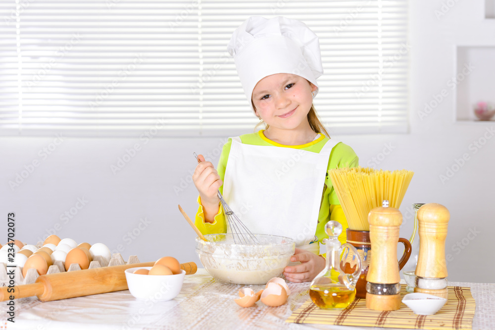 Cute little girl in chef's hat baking cake in the kitchen