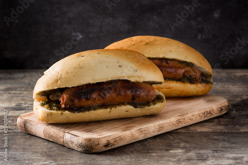 Choripan. Traditional Argentina sandwich with chorizo and chimichurri sauce on wooden table