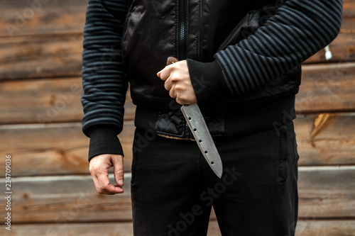 A man, a criminal in black clothes, holds a large knife in his hand. Close-up, copy space. The concept of crime, violation of the law, the criminal.