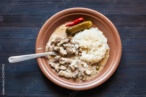 eating of Beef Stroganoff dish from brown plate photo