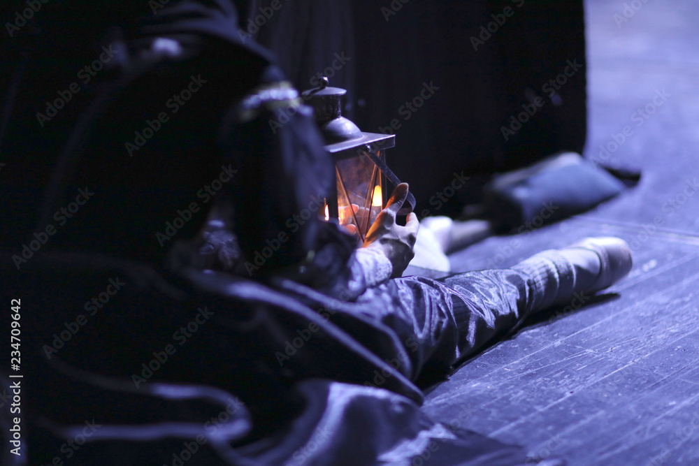 Fototapeta premium Ballerina resting sitting on the floor behind the scenes in stage dress in pointe shoes and old lantern in hand