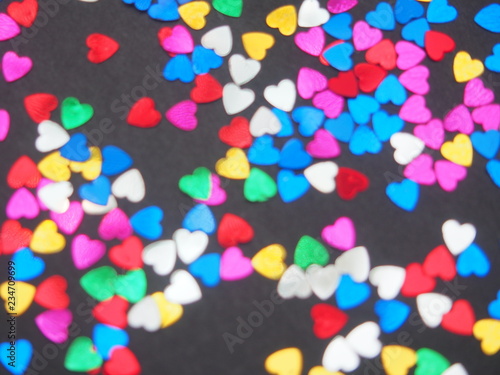 Colorful shiny hearts lie on a black background. Hearts are blurry.