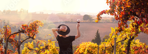 Girl in a hat at sunset and a glass of wine in hand. Nature Italy, hills and grape fields the sunlight. Glare and sun rays in the frame. Free space for text. Copy space. photo