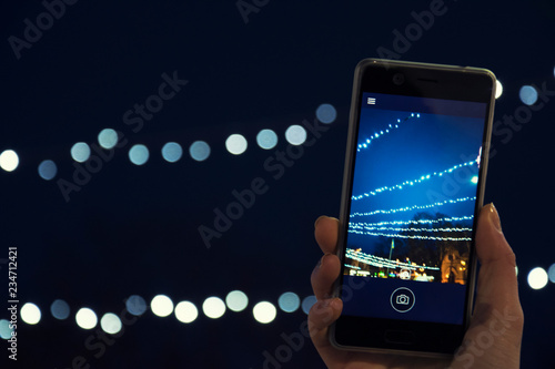 A girl photographing Christmas lights on a smartphone's camera, City, Holidays, New Year