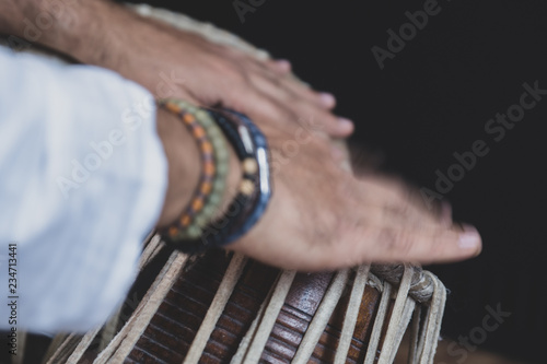 Images of a man's hands (wearing beads) playing the Tabla - Indian classical music percussion instrument - black background.