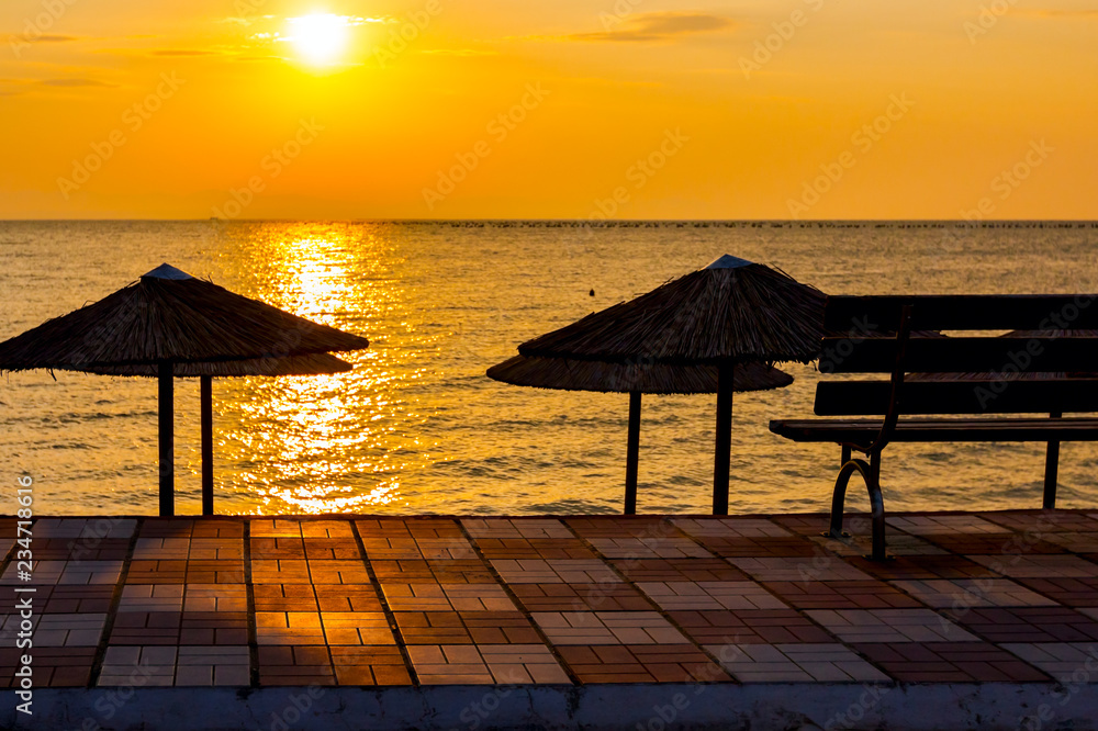 Morning light over empty wooden bench at promenade above public beach next to the coastline Morning light over empty wooden bench at promenade above public beach next to the coastline