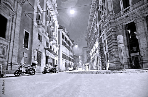 night snowfall in empty street in the historic center of Rome with motorcycles and road surface completely covered by snow