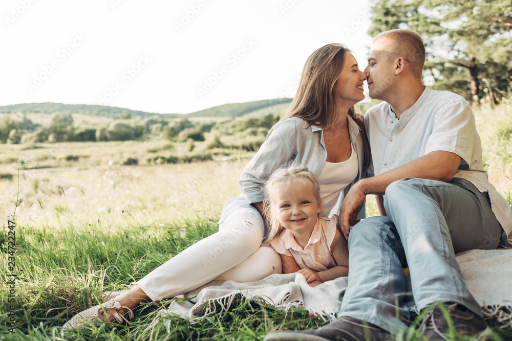 Young Adult Couple with Their Little Daughter Having Fun in the Park Outside the City, Family Weekend Picnic Concept, Three People Enjoying Summer Time Young Adult Couple with Their Little Daughter Having Fun in the Park Outside the City, Family Weekend Picnic Concept, Three People Enjoying Summer Time