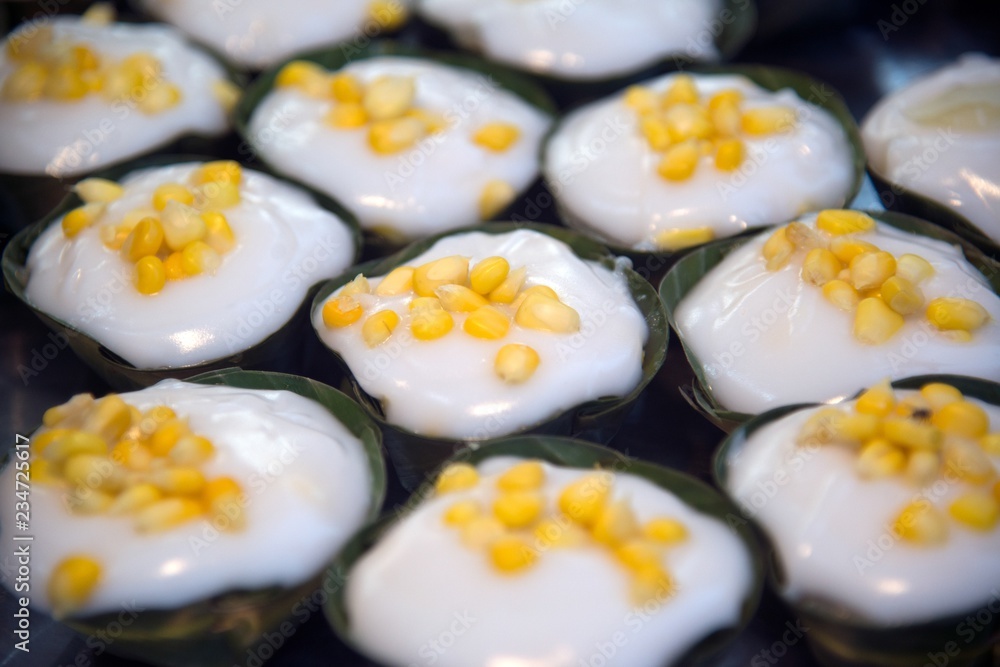 Thai dessert sweet is Creamy Coconut Tapioca and Corn Pudding with Coconut Ta-go topping and wrapped with banana leaves on wooden background. Thai dessert sweet is Creamy Coconut Tapioca and Corn Pudding with Coconut Ta-go topping and wrapped with banana leaves on wooden background.