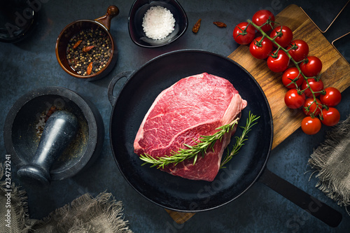 Raw Fresh Marbled Meat Beef on a cast iron pan ready for cooking on a blue concrete background top view.