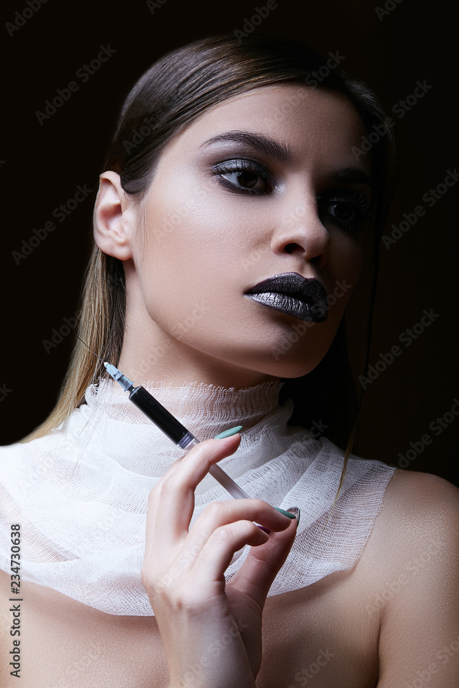 Obraz premium Portrait of a gorgeous dark-haired girl holding a syringe with poison. White translucent neck bandage.