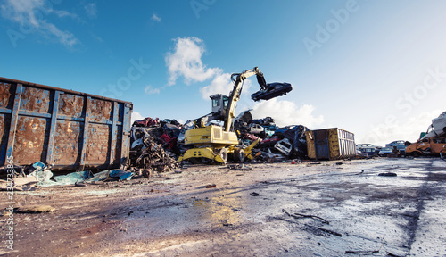 Yellow crane holds broken car on scrapyard recycling center