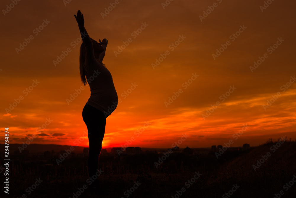 Silhouette of pregnant woman with arms outstretched enjoys spending time outdoor.