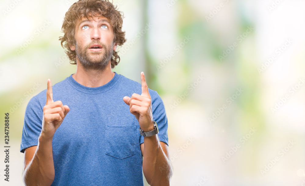 Handsome hispanic model man over isolated background amazed and surprised looking up and pointing with fingers and raised arms. Handsome hispanic model man over isolated background amazed and surprised looking up and pointing with fingers and raised arms.