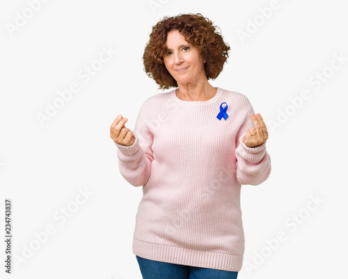 Middle ager senior woman wearing changeable blue color ribbon awareness over isolated background Doing money gesture with hand, asking for salary payment, millionaire business