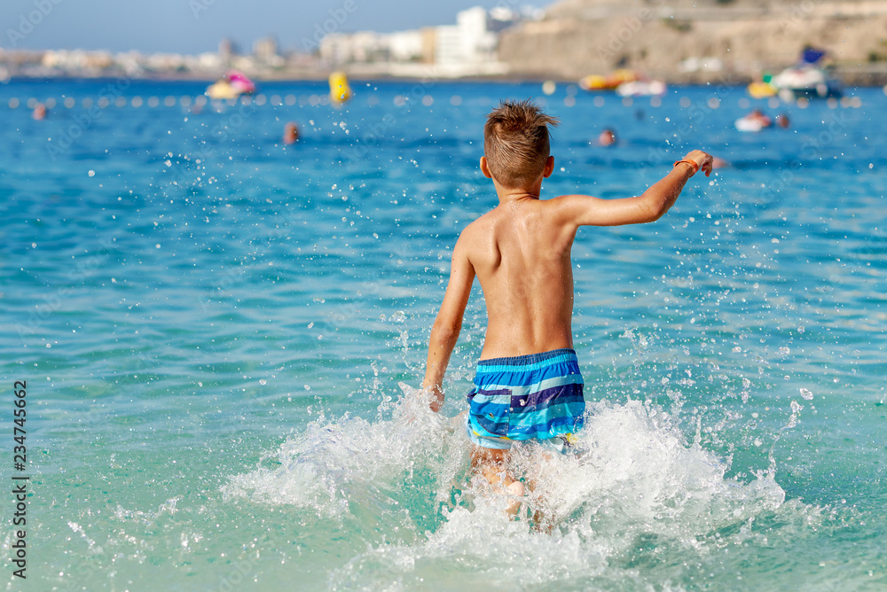 Cute European boy is jumping in to the sea, making numerour splashes around him. He is on his summer vacations.