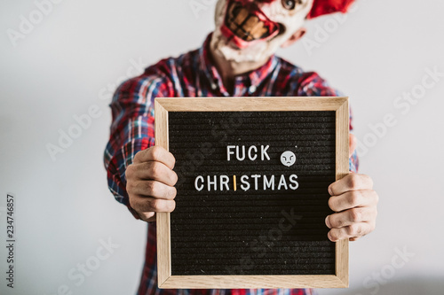 .Young boy dressed as a scary clown in Christmas season. Showing clear hatred for Christmas with a chalkboard that says: "fuck christmas". Lifestyle..
