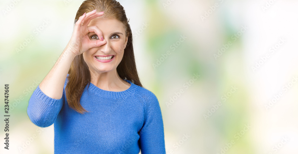 Beautiful middle age mature woman wearing winter sweater over isolated background doing ok gesture with hand smiling, eye looking through fingers with happy face. Beautiful middle age mature woman wearing winter sweater over isolated background doing ok gesture with hand smiling, eye looking through fingers with happy face.