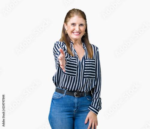 Middle age mature business woman over isolated background smiling friendly offering handshake as greeting and welcoming. Successful business.