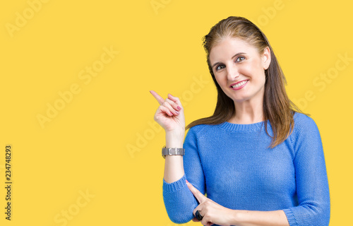 Beautiful middle age mature woman wearing winter sweater over isolated background with a big smile on face  pointing with hand and finger to the side looking at the camera.