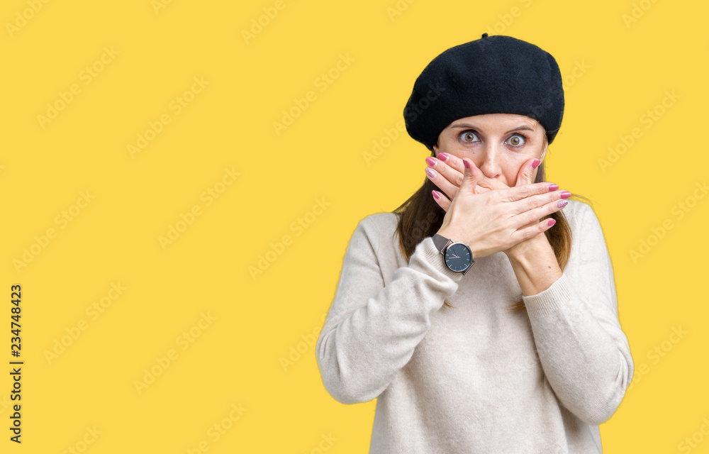 Middle age mature woman wearing winter sweater and beret over isolated background shocked covering mouth with hands for mistake. Secret concept. Middle age mature woman wearing winter sweater and beret over isolated background shocked covering mouth with hands for mistake. Secret concept.