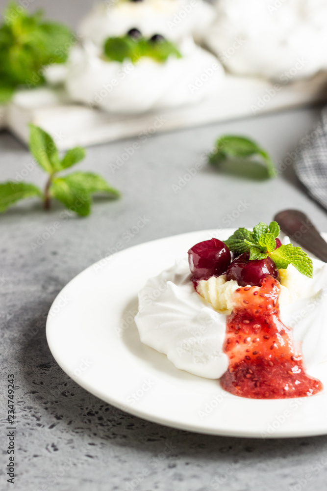 Mini Pavlova or meringue nests with whipped cream, berries and mint, selective focus. Grey concrete background. Copy space. Mini Pavlova or meringue nests with whipped cream, berries and mint, selective focus. Grey concrete background. Copy space.