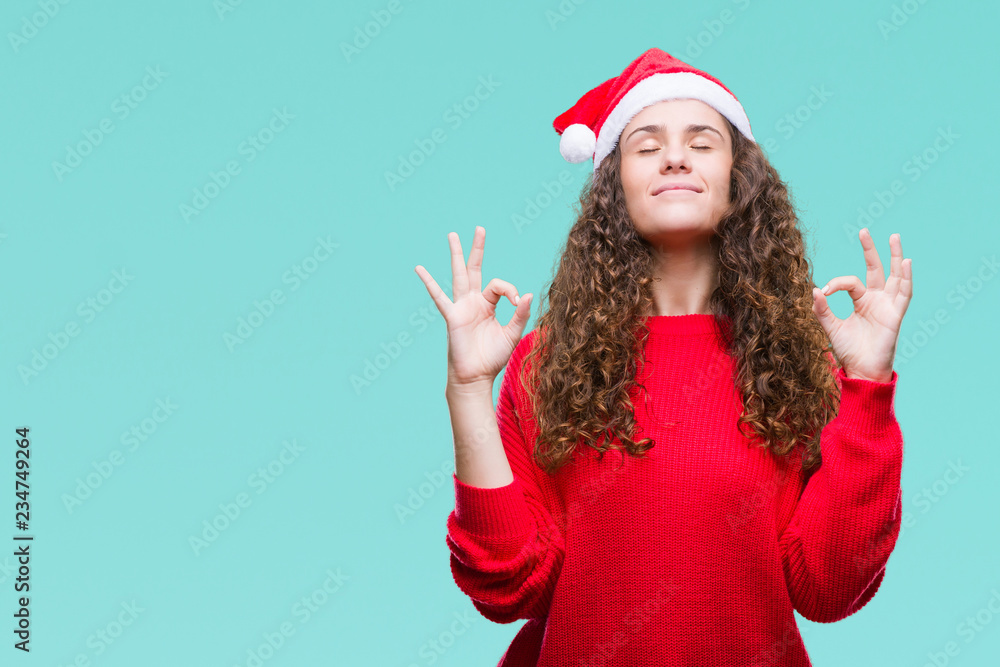 Young brunette girl wearing christmas hat over isolated background relax and smiling with eyes closed doing meditation gesture with fingers. Yoga concept. Young brunette girl wearing christmas hat over isolated background relax and smiling with eyes closed doing meditation gesture with fingers. Yoga concept.