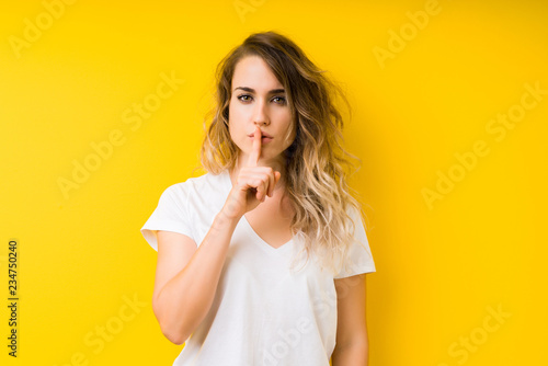 Young beautiful blonde woman over yellow background asking to be quiet with finger on lips. Silence and secret concept.