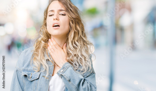 Beautiful young blonde woman wearing denim jacket over isolated background shouting and suffocate because painful strangle. Health problem. Asphyxiate and suicide concept.