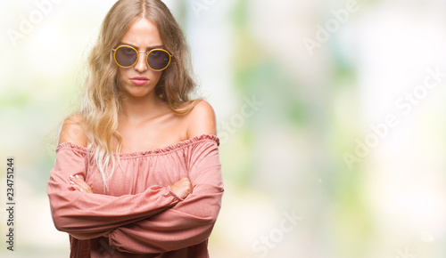 Beautiful young blonde woman wearing retro sunglasses over isolated background skeptic and nervous  disapproving expression on face with crossed arms. Negative person.