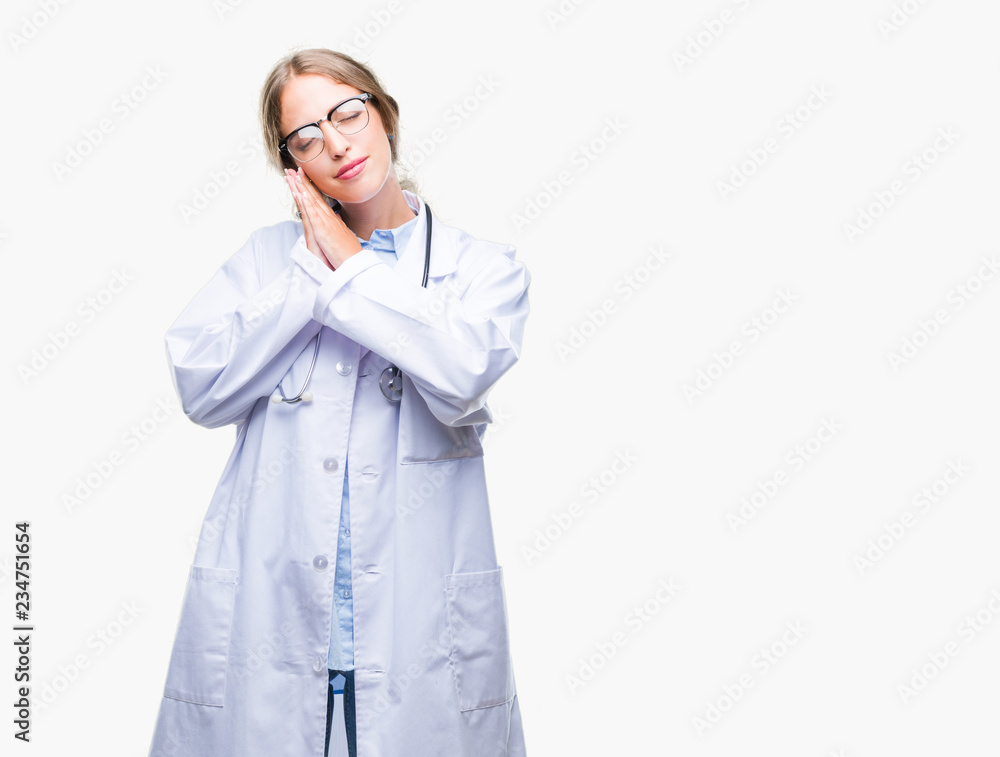 Beautiful young blonde doctor woman wearing medical uniform over isolated background sleeping tired dreaming and posing with hands together while smiling with closed eyes. Beautiful young blonde doctor woman wearing medical uniform over isolated background sleeping tired dreaming and posing with hands together while smiling with closed eyes.
