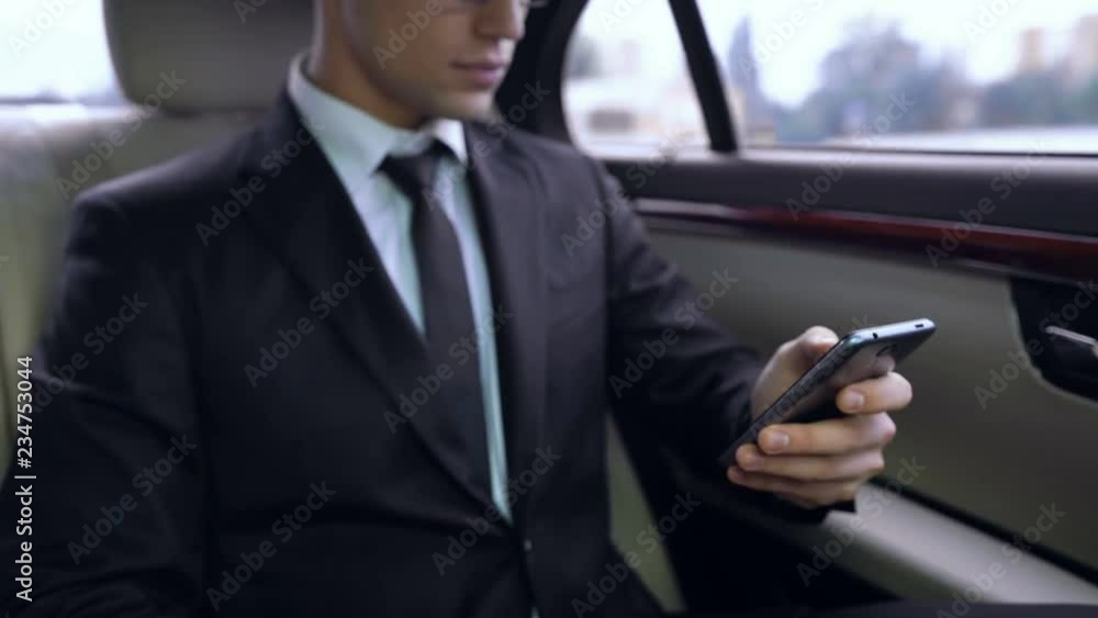 Young male in suit texting on smartphone while riding in personal business car Young male in suit texting on smartphone while riding in personal business car