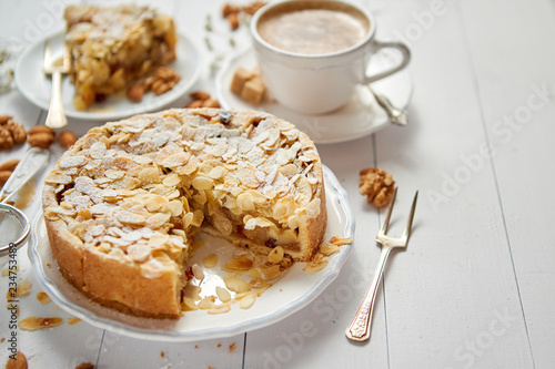 Horizontal shot of a whole round delicious apple cake tart with almond flakes served on wooden table. With coffee in a cup and slice of a pie on soucer. photo