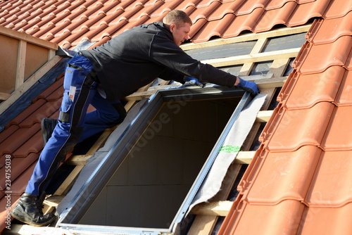 DachdeckerDachdecker baut Dachfenster konzentriert auf dem Dach in rote Dachziegel Dächer ein