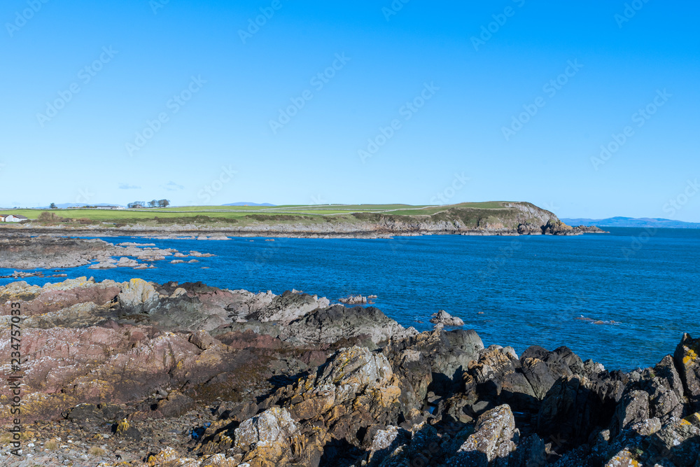 the rugged coastline around Whithorn, Dumfries and Galloway under clear blue skies