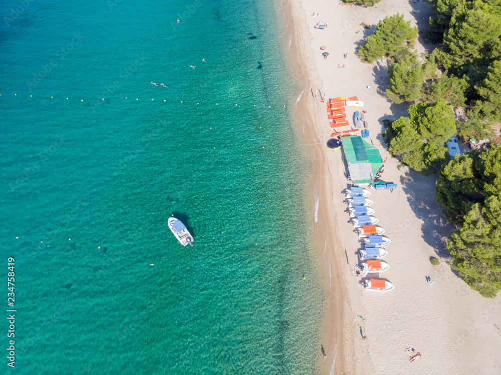 Fototapeta premium Drone aerial view of sea shore, sandy beach and blue water. Boat near beach with lot of sunshades