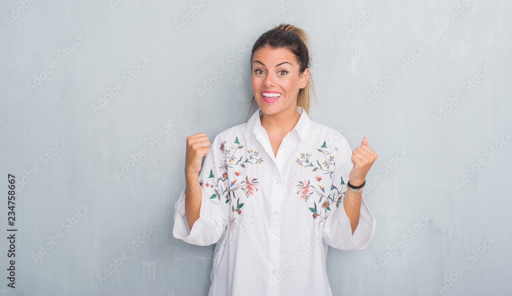 Young adult woman over grunge grey wall wearing flowers shirt celebrating surprised and amazed for success with arms raised and open eyes. Winner concept. Young adult woman over grunge grey wall wearing flowers shirt celebrating surprised and amazed for success with arms raised and open eyes. Winner concept.