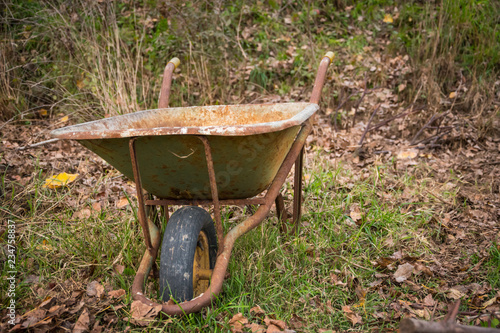 Rusty and abandoned wheelbarrow in a garden, with the wheel still in place.