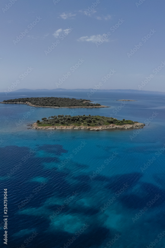 Two small islands surrounded with blue sea water with mountains in background. Drone aerial view