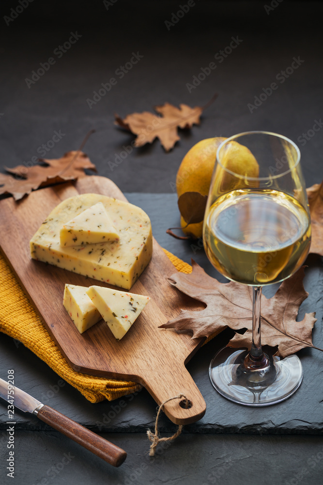 A glass of white wine served with cheese in a cutting board on dark background A glass of white wine served with cheese in a cutting board on dark background
