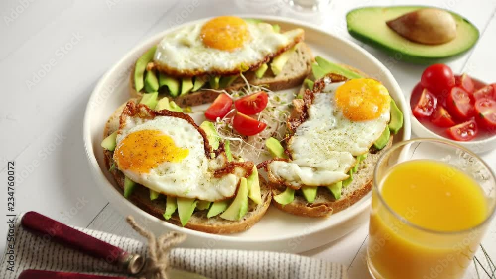 Delicious healthy breakfast with sliced avocado sandwiches with fried egg on top of bread. With orange juice, cherry tomatoes, radish sprouts, salt and peper. Flat lay, top view. Delicious healthy breakfast with sliced avocado sandwiches with fried egg on top of bread. With orange juice, cherry tomatoes, radish sprouts, salt and peper. Flat lay, top view.