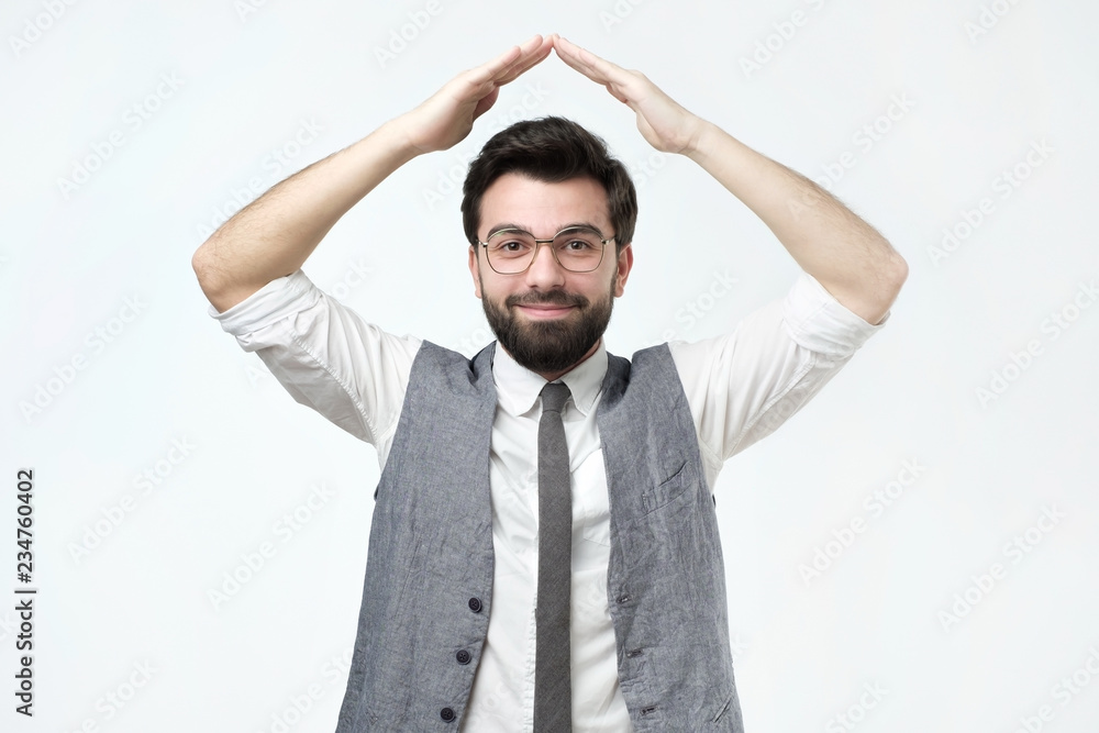 Cheerful man with holding hands over head like a roof house on gray background. To buy a new flat or house. Cheerful man with holding hands over head like a roof house on gray background. To buy a new flat or house.