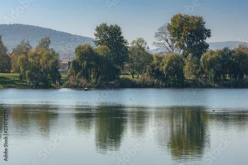 Beautiful rural landscape with a calm water surface. In the distance is a line of forest mountains. In the middle - a strip of green forest, reflected in a blue lake.