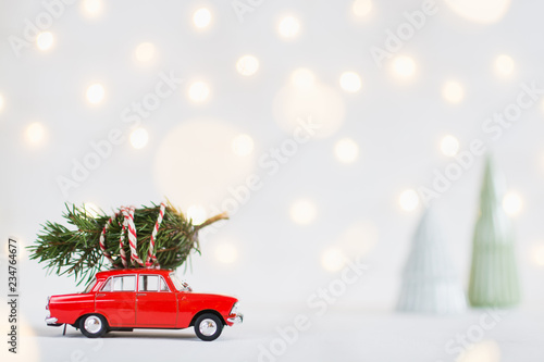 Red toy car with a christmas tree on the roof, garland bokeh on background