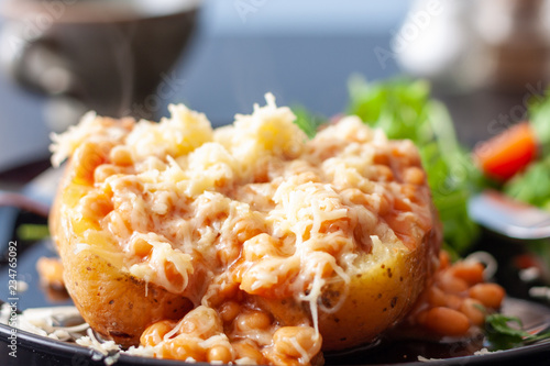 A baked potato topped with baked beans and cheese, served with a salad