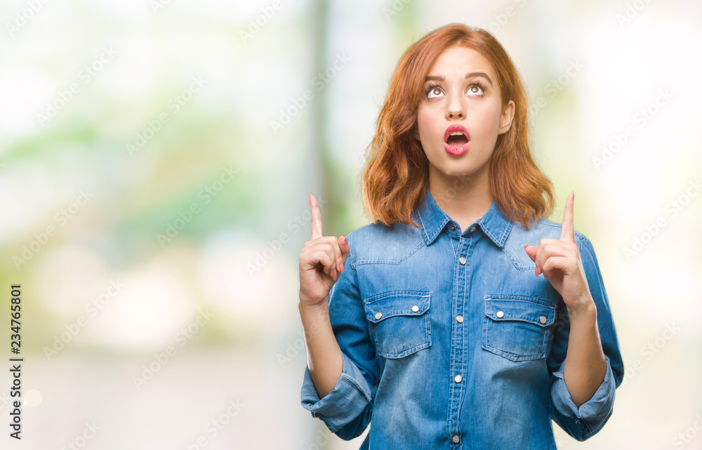 Young beautiful woman over isolated background amazed and surprised looking up and pointing with fingers and raised arms. Young beautiful woman over isolated background amazed and surprised looking up and pointing with fingers and raised arms.