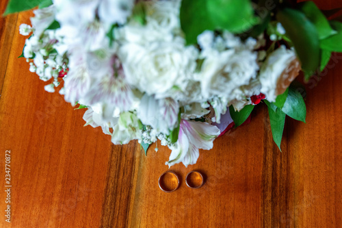 Beautiful wedding rings lie on wooden surface against background of bouquet of flowers. Declaration of love, spring. Wedding card, Valentine's Day greeting. Wedding rings. Wedding day details