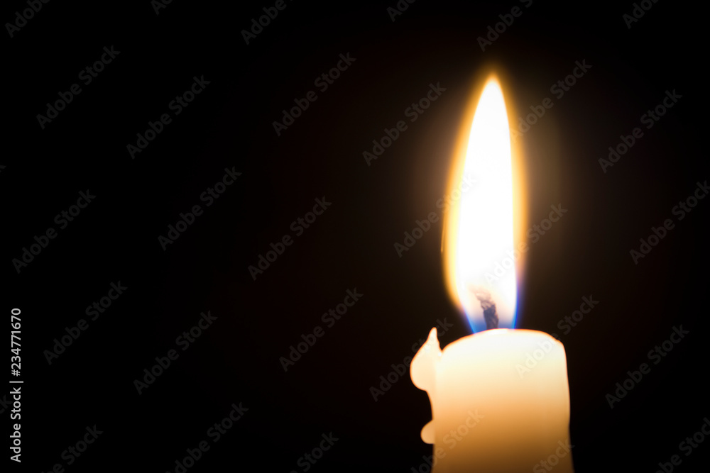 Single burning melted candle with blurred fork of flame against dark background Single burning melted candle with blurred fork of flame against dark background
