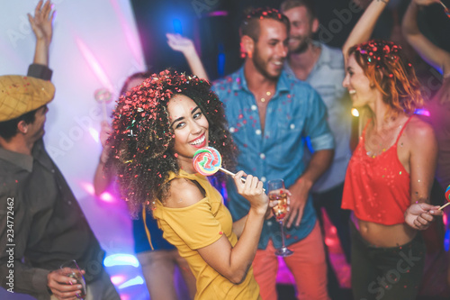 Group of friends dancing and drinking champagne at nightclub - Young happy people having fun and enjoying party eating candy lollipops - Youth friendship lifestyle concept