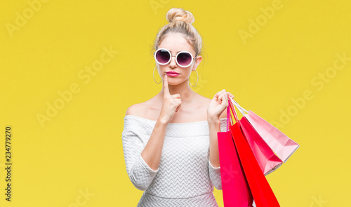 Young beautiful blonde woman holding shopping bags over isolated background serious face thinking about question, very confused idea